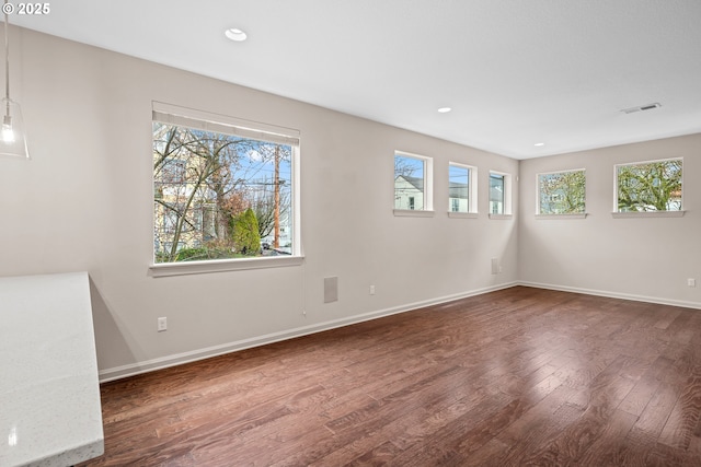 empty room featuring a wealth of natural light, visible vents, baseboards, and wood finished floors