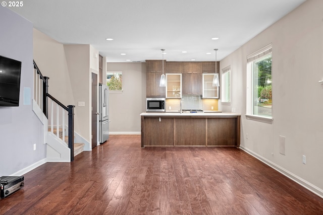 kitchen featuring a peninsula, decorative backsplash, dark wood-type flooring, glass insert cabinets, and appliances with stainless steel finishes