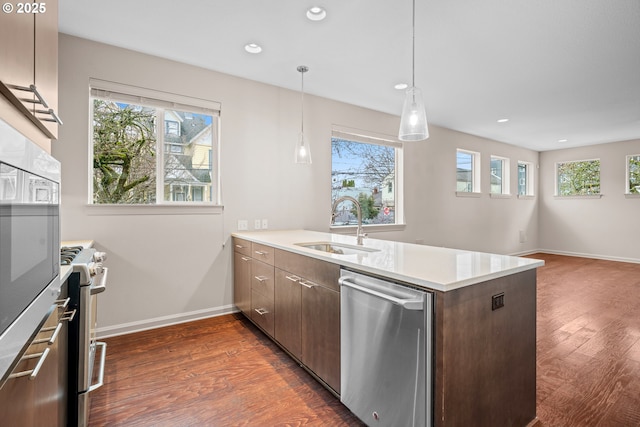 kitchen featuring baseboards, dark wood finished floors, appliances with stainless steel finishes, a peninsula, and a sink