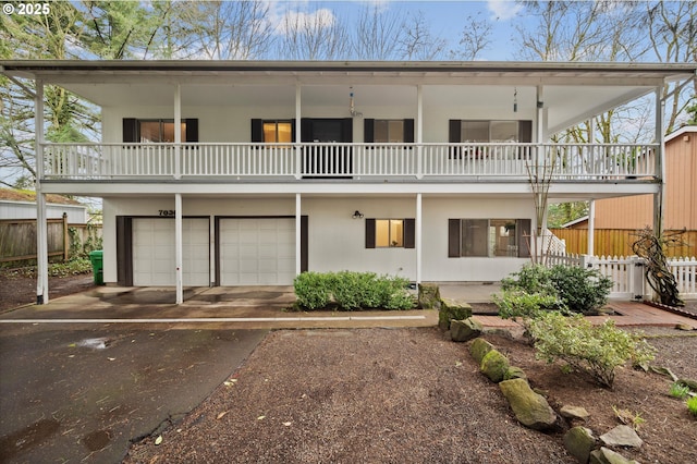 back of property featuring fence, aphalt driveway, stucco siding, a balcony, and an attached garage