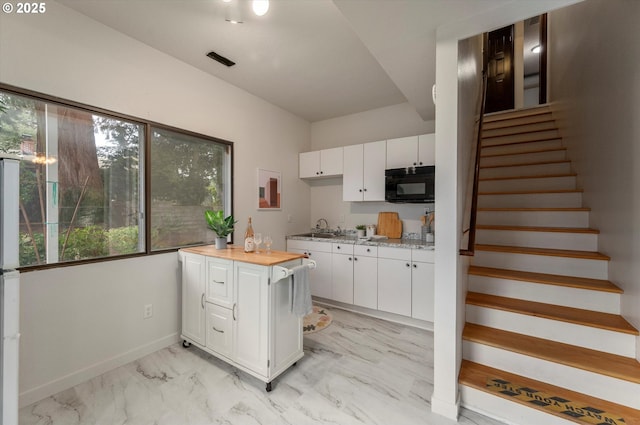 kitchen featuring baseboards, a sink, black microwave, white cabinetry, and marble finish floor