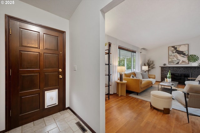 foyer featuring visible vents, baseboards, light wood-type flooring, lofted ceiling, and a stone fireplace