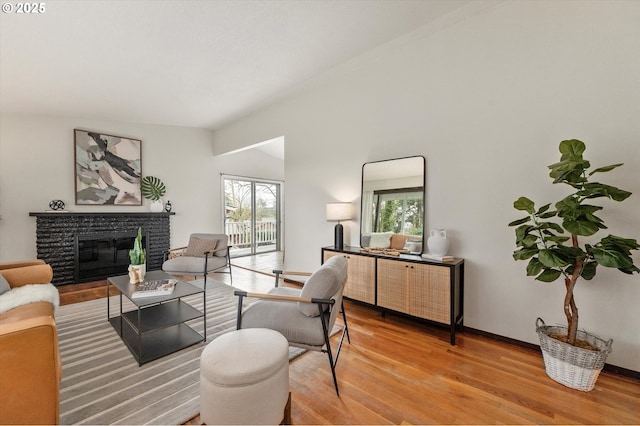 living area with a stone fireplace, vaulted ceiling, light wood-style floors, and baseboards