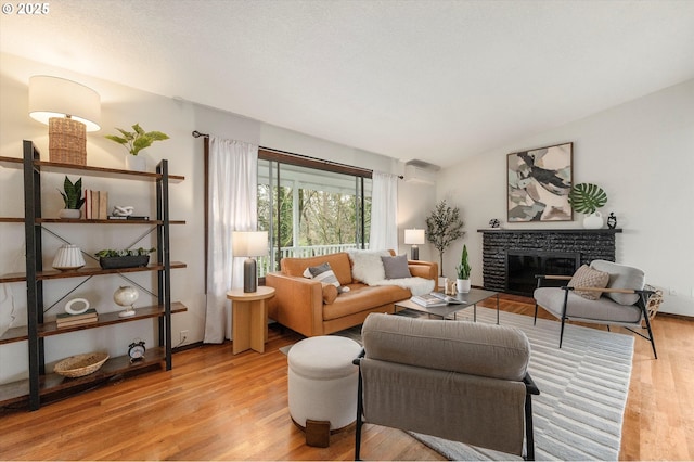 living room with light wood-type flooring, lofted ceiling, and a stone fireplace