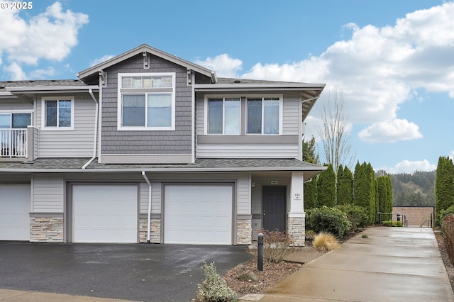 multi unit property featuring driveway, stone siding, roof with shingles, and an attached garage