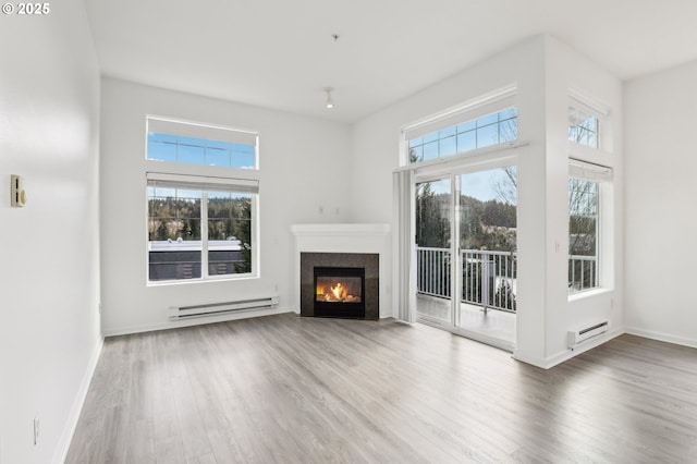 unfurnished living room featuring a healthy amount of sunlight, baseboard heating, and wood finished floors