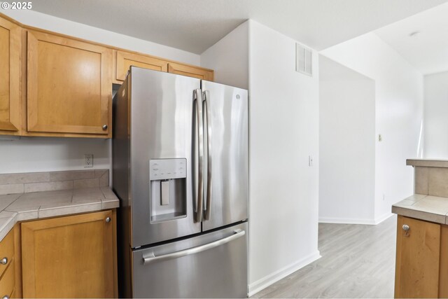 kitchen with light wood finished floors, tile counters, visible vents, brown cabinetry, and stainless steel fridge with ice dispenser