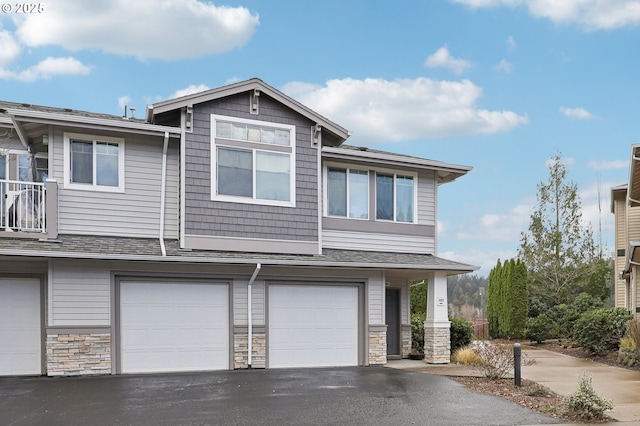 view of property featuring a garage, stone siding, driveway, and roof with shingles