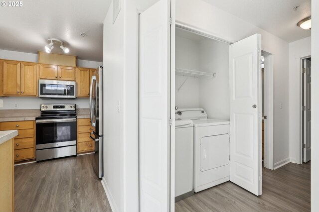 kitchen featuring stainless steel appliances, wood finished floors, washer and clothes dryer, and light countertops