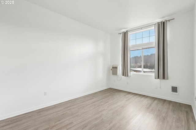 unfurnished room with an AC wall unit, wood finished floors, visible vents, and baseboards