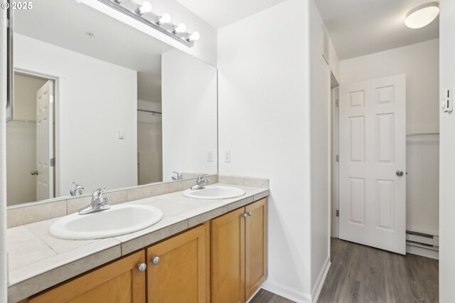 full bath with double vanity, wood finished floors, a baseboard radiator, and a sink