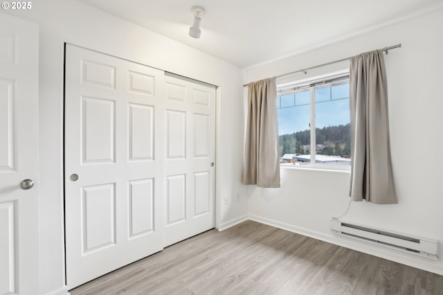 unfurnished bedroom with a baseboard heating unit, a closet, baseboards, and wood finished floors