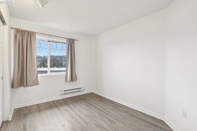 spare room featuring baseboards, a baseboard heating unit, and wood finished floors