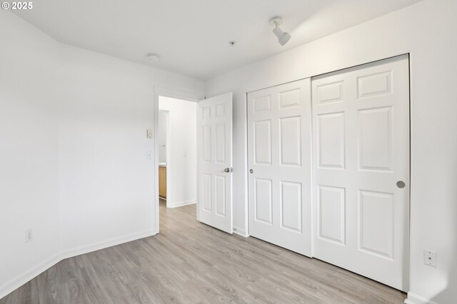 unfurnished bedroom featuring a closet, light wood-type flooring, and baseboards