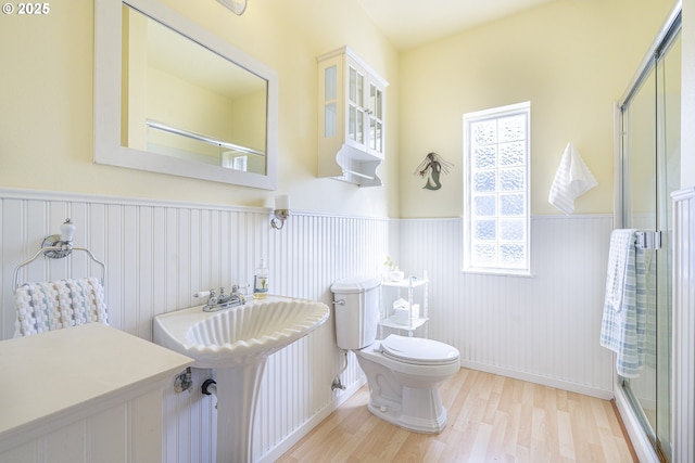 bathroom with wood finished floors, toilet, wainscoting, a stall shower, and a sink