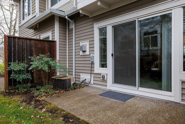 view of exterior entry featuring a patio, central AC, and fence