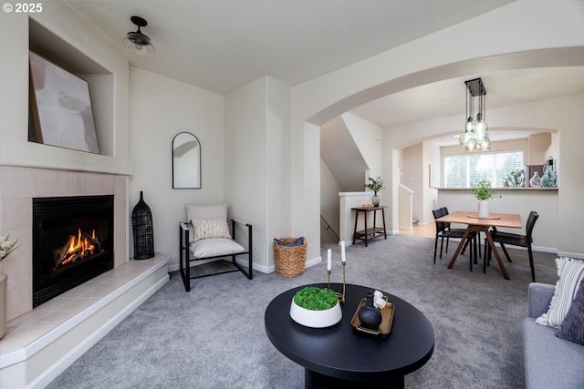 carpeted living area featuring baseboards, arched walkways, and a tile fireplace