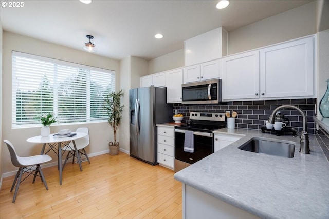 kitchen featuring a sink, stainless steel appliances, white cabinets, light wood-style floors, and backsplash