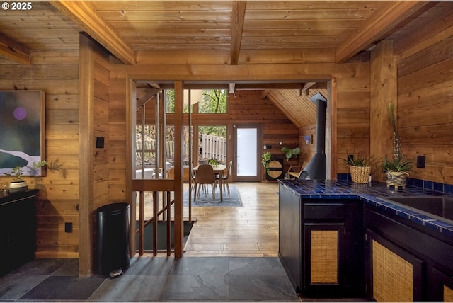 kitchen with tile countertops, wood walls, wooden ceiling, and a wood stove