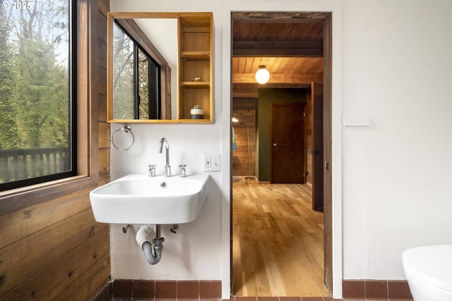 half bathroom with wood finished floors, wood ceiling, a healthy amount of sunlight, and a sink