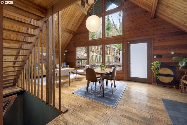 dining area featuring beamed ceiling, high vaulted ceiling, light wood-style floors, wooden walls, and wood ceiling