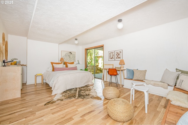 bedroom featuring access to exterior, wood finished floors, and a textured ceiling