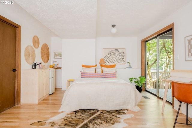 bedroom with a textured ceiling, light wood-style floors, access to outside, and freestanding refrigerator