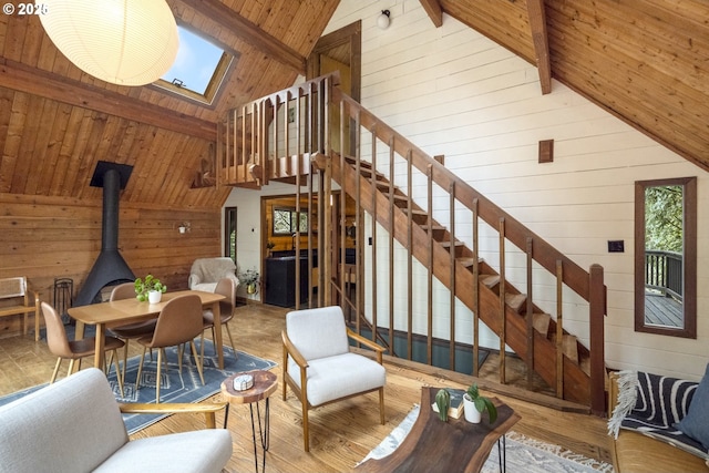 living area featuring a wood stove, beam ceiling, wooden walls, wooden ceiling, and stairs