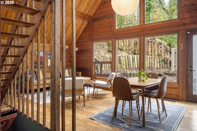 interior space featuring stairway, light wood-style floors, wood walls, and high vaulted ceiling