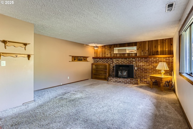 unfurnished living room featuring a textured ceiling, wood walls, carpet floors, and a wood stove