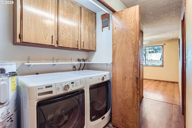 laundry area with wood-type flooring, washing machine and clothes dryer, cabinets, a textured ceiling, and water heater