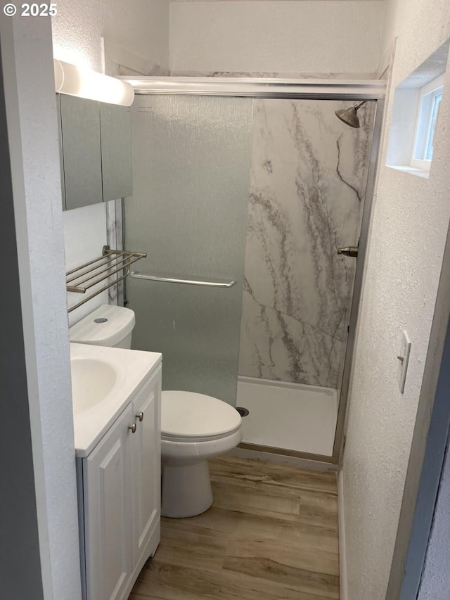 bathroom featuring vanity, wood finished floors, a shower stall, toilet, and a textured wall