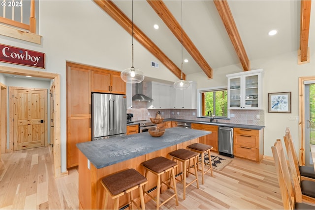 kitchen featuring wall chimney exhaust hood, a center island, hanging light fixtures, white cabinetry, and appliances with stainless steel finishes