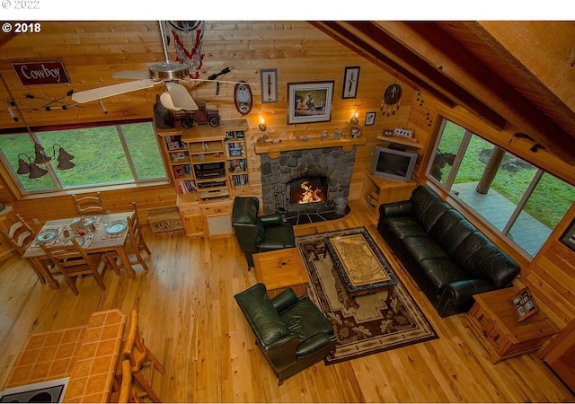 living room featuring ceiling fan, wood walls, a fireplace, and wood-type flooring