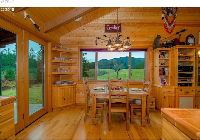 dining room with lofted ceiling with beams, wood walls, light hardwood / wood-style floors, a notable chandelier, and a mountain view