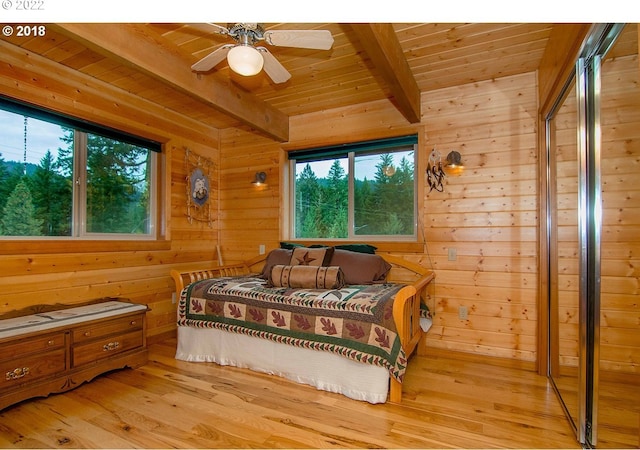 bedroom featuring wood walls, ceiling fan, light hardwood / wood-style floors, and beamed ceiling