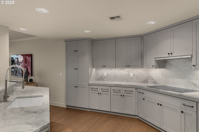 kitchen with light stone counters, black electric stovetop, gray cabinets, light wood-style floors, and a sink