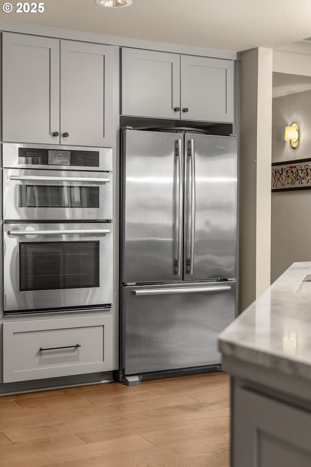 kitchen with gray cabinetry, stainless steel appliances, wood finished floors, and light countertops