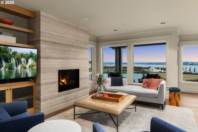 living area featuring recessed lighting, a large fireplace, a water view, and wood finished floors