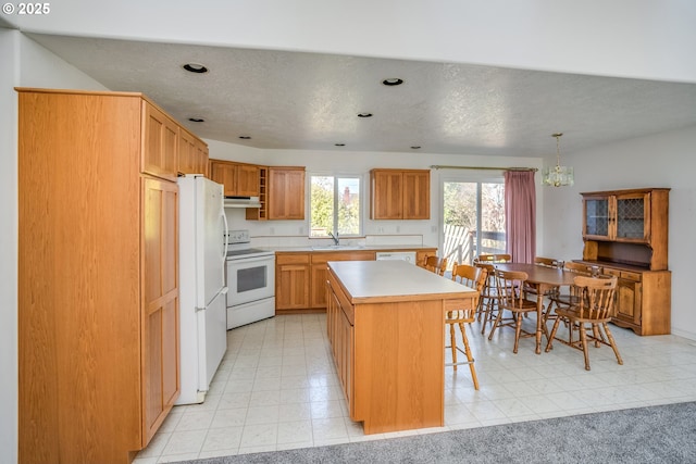 kitchen with a sink, under cabinet range hood, a center island, white appliances, and light countertops