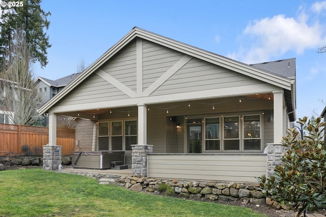 back of property with a yard, fence, and a hot tub