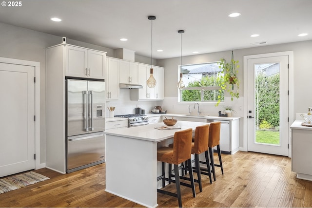 kitchen featuring pendant lighting, a center island, high end appliances, white cabinets, and light wood-type flooring