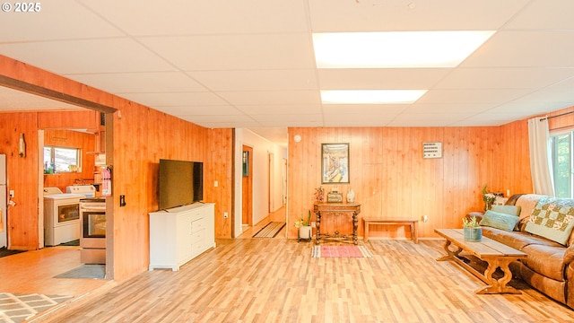 living room featuring washer / dryer, light hardwood / wood-style flooring, wooden walls, and a paneled ceiling