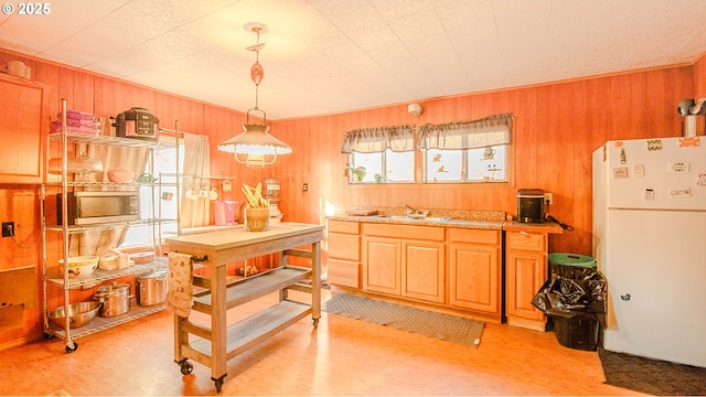 kitchen featuring wood walls, decorative light fixtures, sink, white fridge, and light wood-type flooring