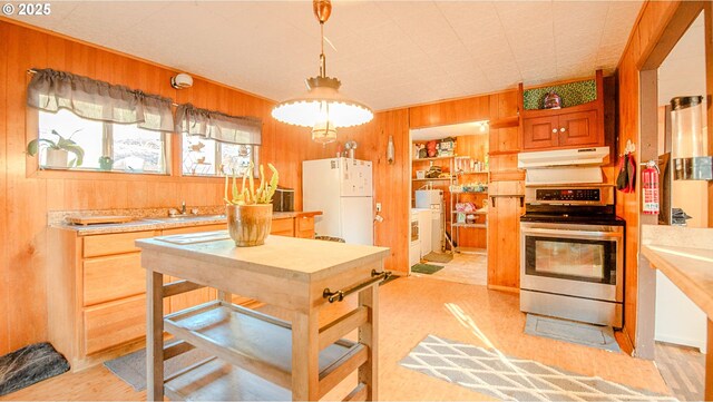 kitchen featuring wood walls, sink, hanging light fixtures, white fridge, and stainless steel range