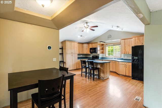 kitchen featuring black appliances, a sink, light wood-style flooring, light brown cabinets, and lofted ceiling