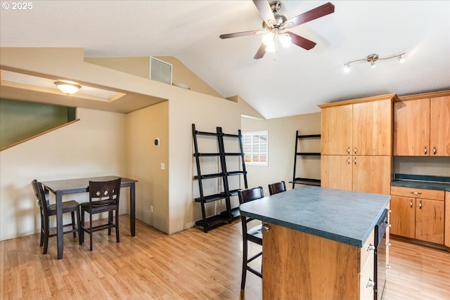 kitchen featuring a kitchen bar, light wood-style floors, dark countertops, a center island, and lofted ceiling