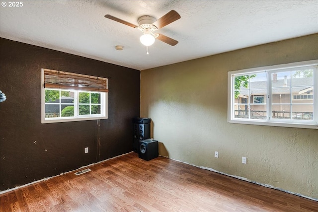 spare room featuring healthy amount of natural light, ceiling fan, wood finished floors, a textured wall, and a textured ceiling