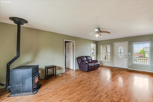 living room with a wood stove, light wood-style floors, ceiling fan, and baseboards