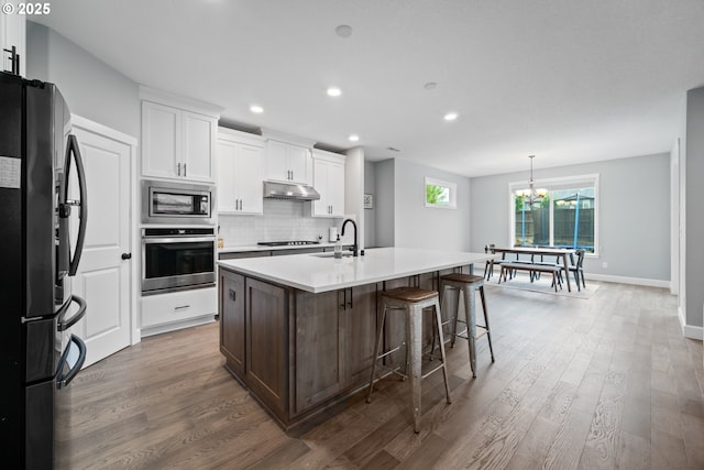 4342 S 16th Way, Ridgefield, WA 98642 - kitchen with appliances with stainless steel finishes, under cabinet range hood, a sink, a chandelier, and wood finished floors
